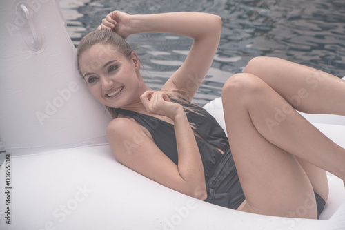 beautiful young woman in a black swimsuit relaxes and sits on a swan-shaped rubber float at a resort hotel swimming pool.