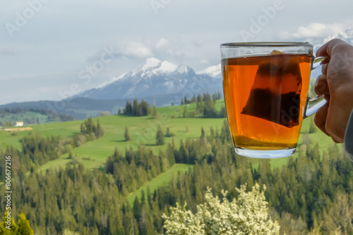 Przezroczysty kubek z herbata w torebce trzymany na tle panoramy Tatr 