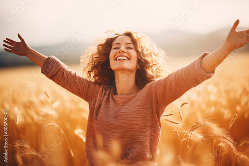 Joyful woman with curly hair spreading arms wide open in a golden wheat field, expressing freedom and happiness.