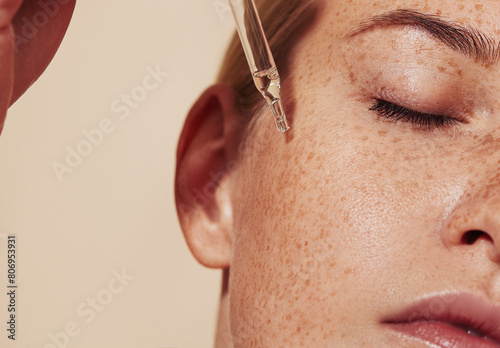 Close-up highly detailed shot of female skin with freckles and pipette with serum. Cropped shot of young woman with smooth perfect skin applying liquid serum on face.