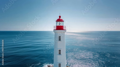  A red-and-white lighthouse atop a cliff overlooks a body of water, backed by a blue sky