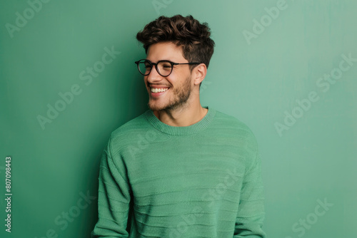 A man wearing glasses and a green sweater laughs candidly, exuding a warm, relaxed and positive vibe
