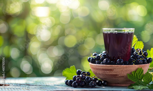 Black currant berries in a wooden bowl On a blurred green background With elements of 1 glass of cool blackcurrant juice. Healthy food concept.