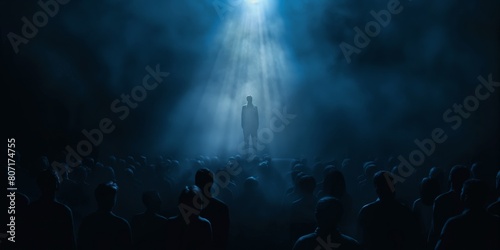 A single enigmatic figure is highlighted by a spotlight on a stage in front of a silhouetted crowd, evoking intrigue