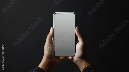  In a tight shot, a person's hands firmly grip a mobile mockup with a blank screen against a black backdrop, the device positioned at eye level