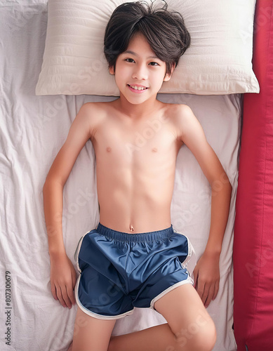 Shirtless, cute Japanese boy lying on a bed.