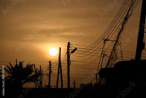 Low setting full round sun with electricity and telephone cable wires in silhouette, Accra, Ghana