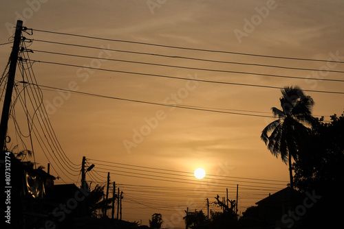 Low setting full round sun framed with electricity and telephone cable wires and palm trees in silhouette, Accra, Ghana