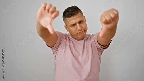 Cool young latin guy so totally thumbs down! he's standing isolated on white background, expressing negative vibe, doing thumb down gesture like a bad sign