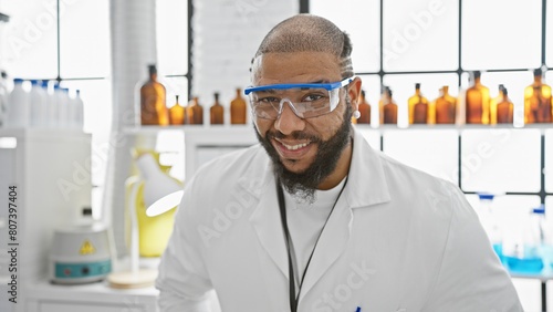 Handsome african american male scientist with beard wearing lab coat and protective glasses in laboratory.