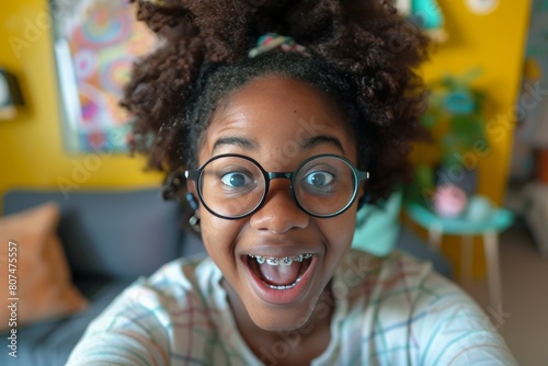 Phone selfie made by smiling african american girl wearing glasses and braces, natural soft light and colors in her room on the background