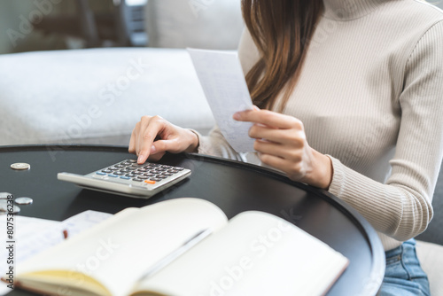 Stressed asian young business woman, employee using calculator to calculate expenses of monthly, hand holding bills and receipt for to payment on table at home. Financial, finance of banking concept.