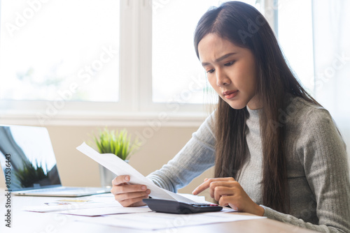 Business financial concept, owe asian young woman sitting stressed, hand calculate expense, cost or budget on table at home from invoice or bill have no money to pay mortgage or loan, debt bankruptcy.