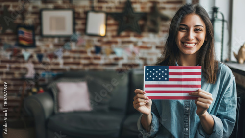 A smiling young woman proudly displays the U.S. flag at a cozy home setting.
