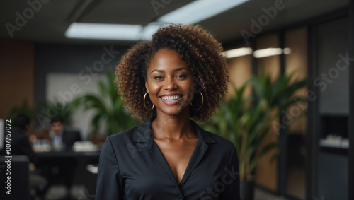 Bella donna di origini africane con capelli ricci sorride in un moderno ufficio con abito elegante