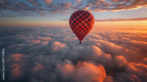 A hot air balloon with a checkered pattern flies above the clouds at sunrise, creating a breathtaking scene of beauty and freedom.