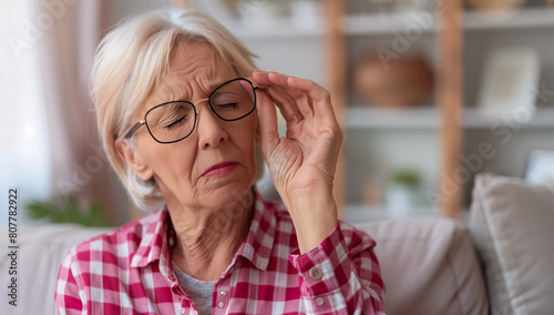 Senior lady in glasses with a pained expression holding her forehead, suggesting a headache or discomfort.