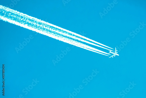 An airplane with four clear lines of contrails against a cloudless sky, the grace of flight. Travel symbol. technological progress, air pollution by chemical sprays from the air