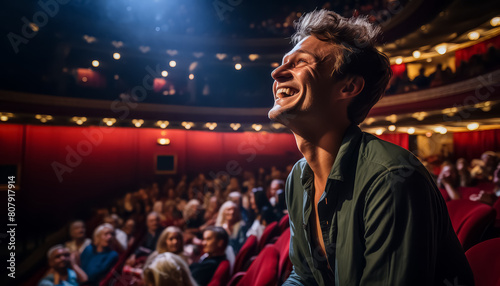 A man is smiling in a theater with a crowd of people watching him