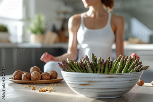 A young woman in a white sports bra and leggings meditates and doing yoga in a light room, with a bowl of asparagus and fruits nearby. Healthy living and mindfulness for wellness content.