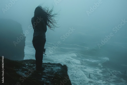 A mysterious silhouette of a woman with her hair blowing in the wind, standing on a cliff overlooking a foggy sea
