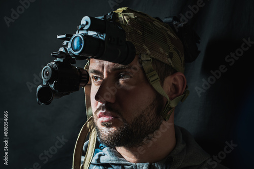Portrait of a military man with a beard with a binocular night vision device on his head.