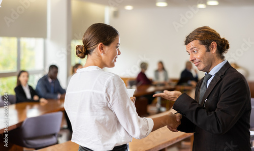 Positive young woman shaking hand of businessman employer during meeting in company office.