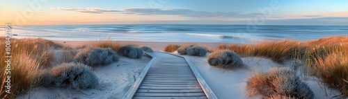 The boardwalk, adorned with only a handful of shrubs along its path, guides visitors towards a pristine sandy beach and the vast expanse of the ocean as the sun sets