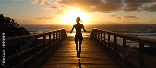 silhouette of sports woman running on wooden boardwalk at sunrise beach