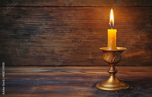 An antique brass candle stand set against a backdrop of dark timber with a burning candlestick