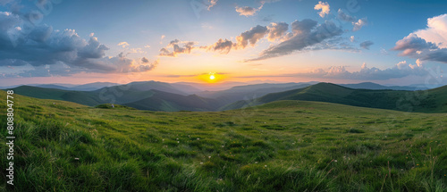 Beautiful nature summer scene with green grass on mountains hills and sunset cloudy sky over mountains as background looking at wide angle lens