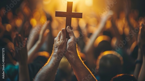 Glorification concept, hand holding up cross in front of large crowd of people their hands raised in worship, forgiveness love joy peace unity