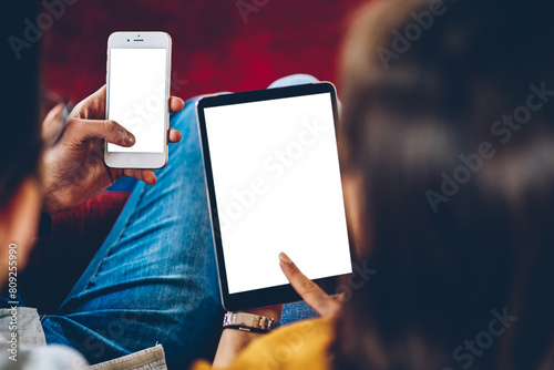 Cropped back view of young marriage reading news on internet websites and sharing multimedia from smartphone on touch pad with copy space display.Young people checking mail and downloading media