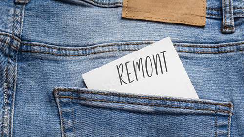  White card with a handwritten inscription "Remont", inserted into the pocket of blue pants jeasnow (selective focus), translation: renovation