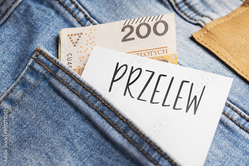  White card with a handwritten inscription "Przelew", put into the pocket of blue pants jeasnow, next to Polish banknotes PLN (selective focus), translation: transfer