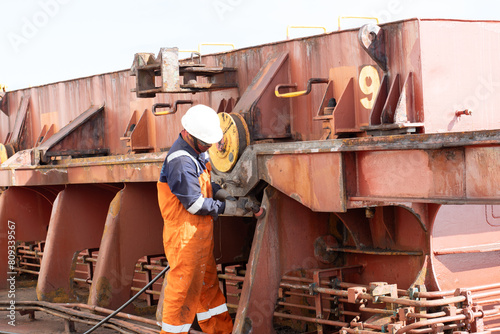 deck crew member of ship preparing hatch coaming surface plate uning pnumatic buffing grinder