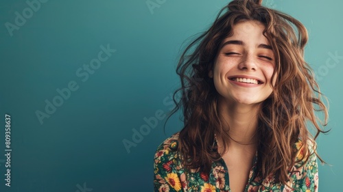 Joyful young woman with curly hair smiling closed eyes against teal background