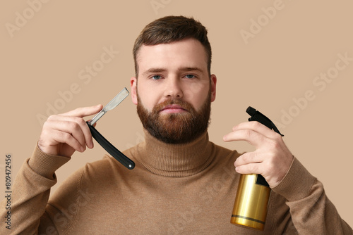 Young bearded man with open razor and sprayer on color background