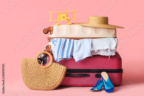 Suitcases with female clothes, beach accessories and toy plane on color background