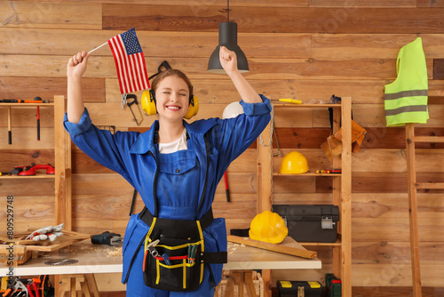 Young female carpenter with earmuffs and USA flag in workshop. Labor Day celebration