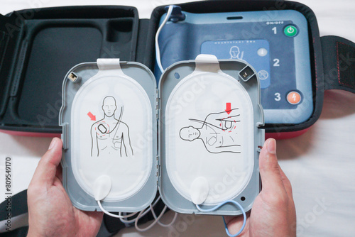 Automatic external defibrillator. Portable defibrillator on a wooden table. Defibrillator for medical care. Device for provision of emergency medical care. Automatic cardioverter with nursing manual