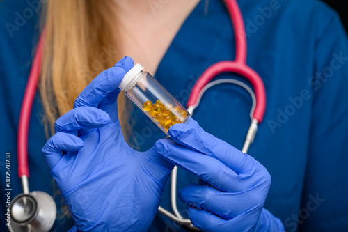 Lekarz trzyma w dloni fiolkę z małymi kapsułkami 