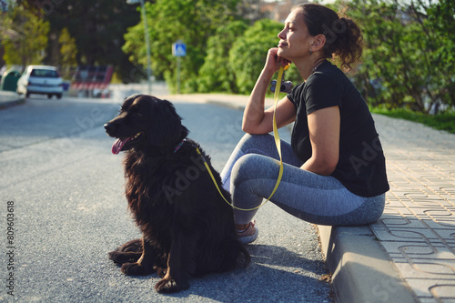 Side portrait of a thoughtful young adult woman sitting on the parapet, dreamily looking into the distance while taking her pet for a walk on the nature. People and animals concept