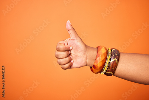 Hand, thumbs up and person with arm on orange background for thank you or confirm with gesture or sign. Good news, expression and positive with yes or thanks with win in studio for agreement.