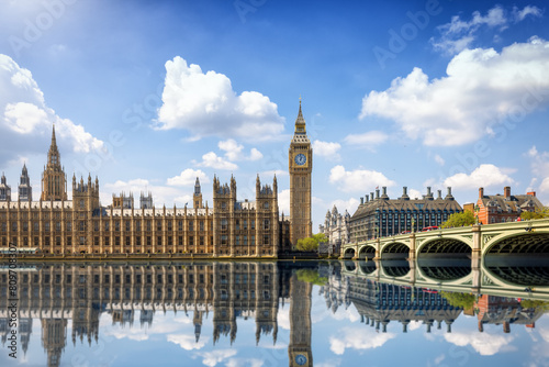 Summer view of the Westminster Bridge and Palace with Big Ben clocktower in London, England, with sun, clouds and reflections in the river Thames