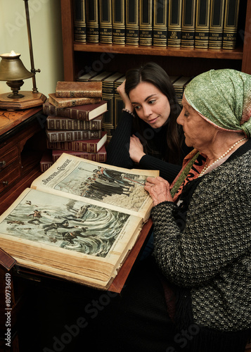 Foto scattata ad una nonna con sua nipote mentre leggono una raccolta di libri antichi.