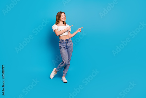 Full size photo of nice young girl point fingers empty space wear top isolated on blue color background