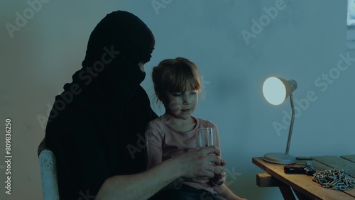 Kidnapper holding the girl hostage in his arms while giving a glass of water for her. Copy space. Kidnapping. Child abduction concept. 