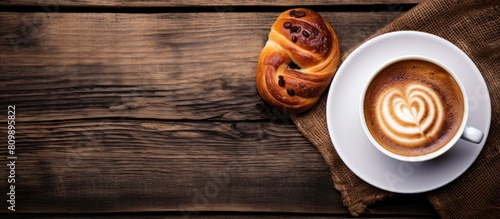 A top down view of a cup of coffee or cappuccino alongside a plate of traditional Swedish cinnamon buns known as kanelbulle The image is set against a wooden background offering ample copy space