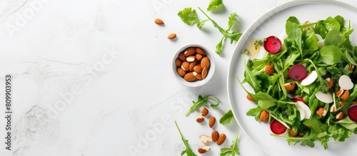 A healthy vegan salad with a mix of ingredients including radish lettuce mangold parsley arugula almonds salt tasty balsamic and pepper is presented on a white plate in a flat lay style leaving ample